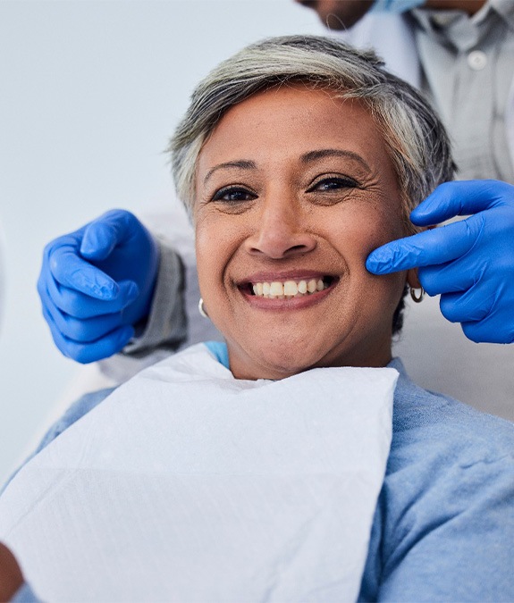 Woman smiling while holding small mirror with dentist