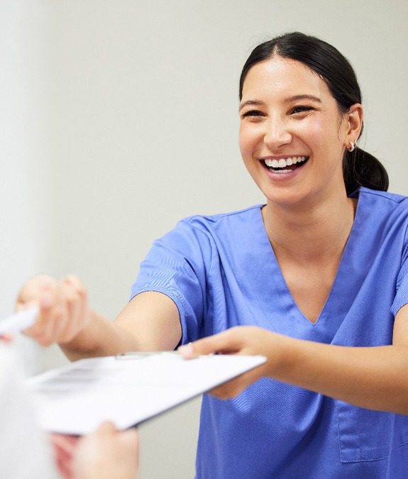 Dental assistant smiling while handing patient form